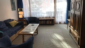 Een woonkamer met een bank, fauteuil, bijzettafeltje en een boekenkast.