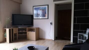 A living room with a flat-screen TV on a wooden stand, a framed picture on the wall, and a doorway leading to another room.