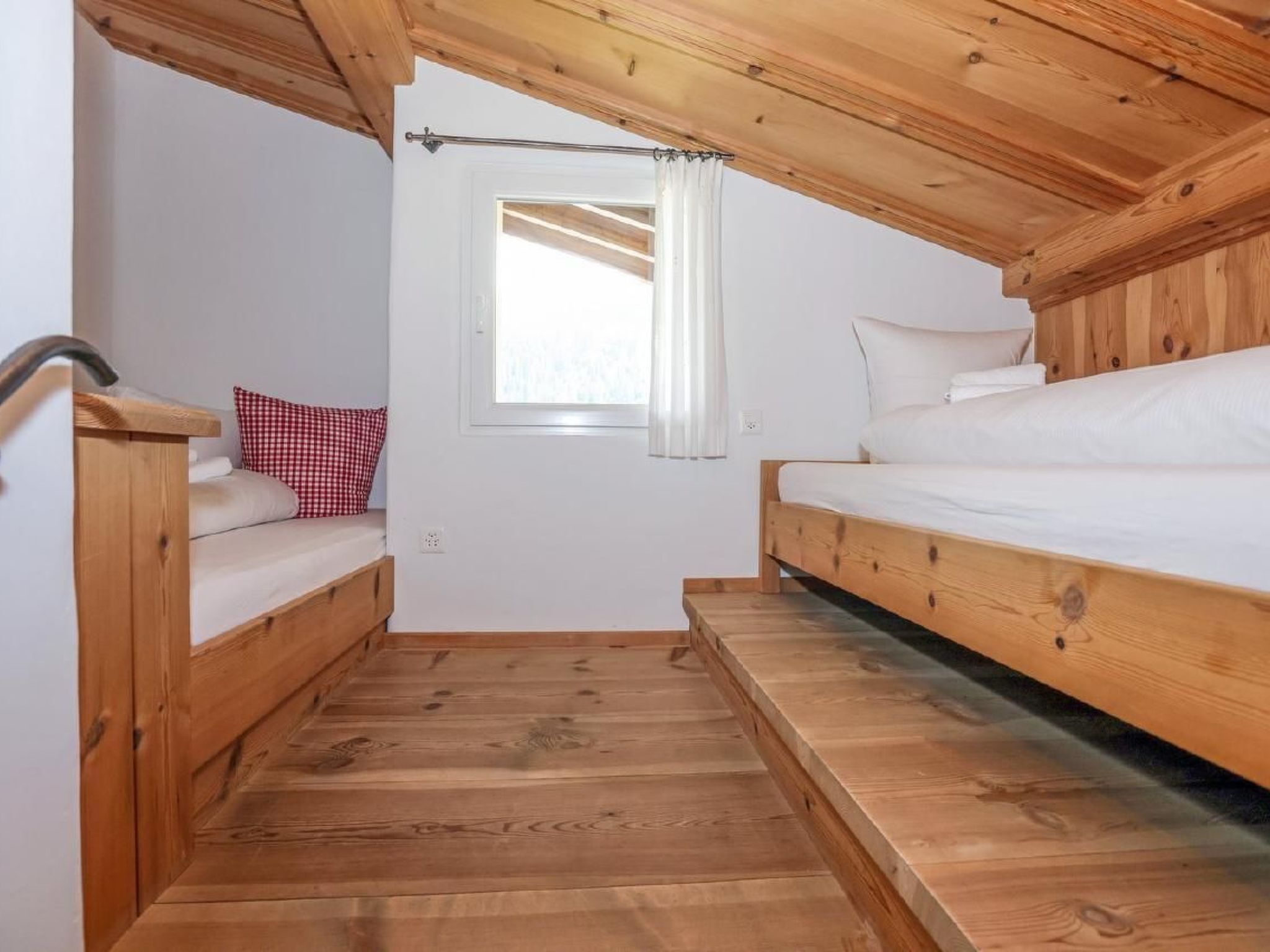Une petite pièce en bois, avec deux lits superposés, une fenêtre avec des rideaux et une petite porte.