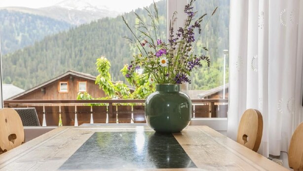 Une table en bois avec un vase de fleurs devant une fenêtre donnant sur une vue de montagne.