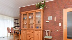 A wooden cabinet with glass doors, a dining table with chairs, and a door with a handle. - Strandnahes Ferienhaus mit Kinderspielplatz by Interhome (Bensersiel)