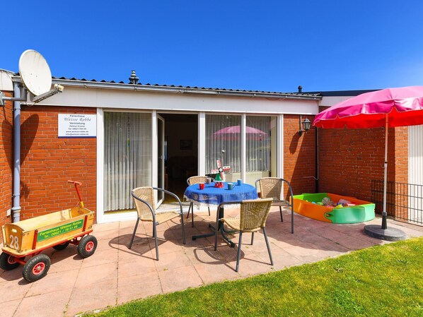 A patio area with a table and chairs, a small play area, and a wooden cart. - Strandnahes Ferienhaus mit Kinderspielplatz by Interhome (Bensersiel)