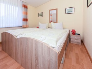 A bedroom with a wooden bed, a bedside table with a lamp, and two framed pictures on the wall. - Strandnahes Ferienhaus mit Kinderspielplatz by Interhome (Bensersiel)