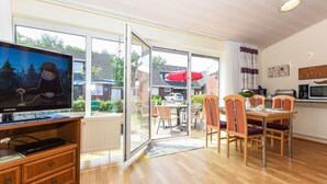 A modern living room with a television, wooden furniture, a dining area, and a sliding glass door leading to an outdoor space. - Strandnahes Ferienhaus mit Kinderspielplatz by Interhome (Bensersiel)