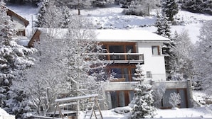 En bygning med flere etager og balkon, omgivet af sneklædte træer og en træterrasse.
