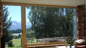 Et værelse med en stor skydedør, der fører ud til en balkon med udsigt til træer og bjerge.