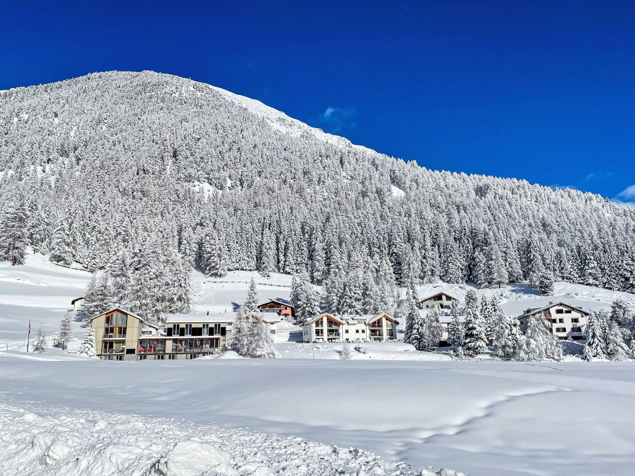 A snow-covered mountain with a clear blue sky. There are several buildings with multiple stories and a variety of architectural styles.