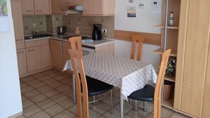 A compact kitchen with wooden cabinets, a coffee maker, and a dining table with chairs. - Vacation home Körner by Interhome (Dahme)