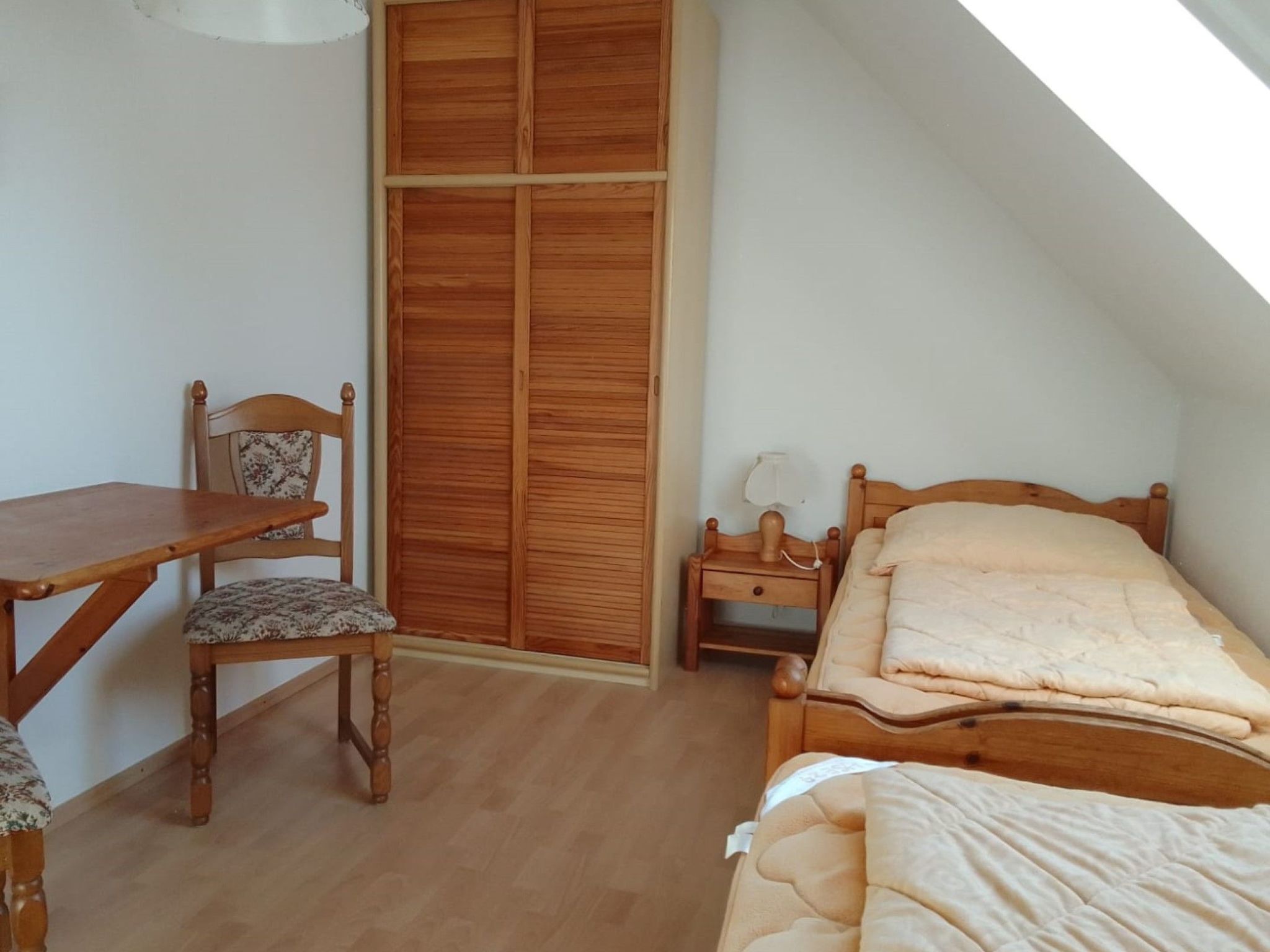 Ein Schlafzimmer mit einem hölzernen Bett, einem Nachttisch aus Holz, einem Holzstuhl, einem Schreibtisch und einem Holzschrank.