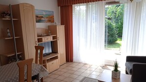 A living room with a TV, a dining table, chairs, a sofa, a cabinet, and a window with curtains. - Vacation home Körner by Interhome (Dahme)
