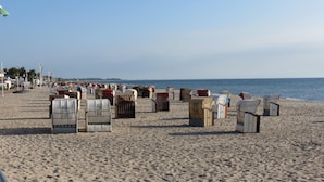 A beach with rows of numbered beach chairs and umbrellas, a clear sky, and a calm sea. - Vacation home Körner by Interhome (Dahme)