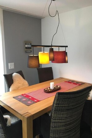 A dining area with a wooden table, black chairs, a red placemat, and a hanging light fixture with three lamps. - Fewo mit Bergblick by Interhome (Savognin)