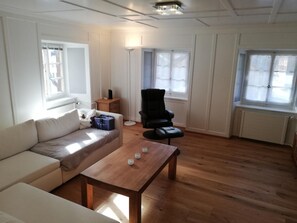 Ein Wohnzimmer mit einem Holztisch, einem beigefarbenen Sofa, einem schwarzen Sessel und einem kleinen Holztisch mit einer Lampe.