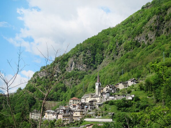 Ein Dorf an einem Hang mit traditionellen Häusern, einer Kirche mit einem hohen Kirchturm und einer kleinen Brücke.