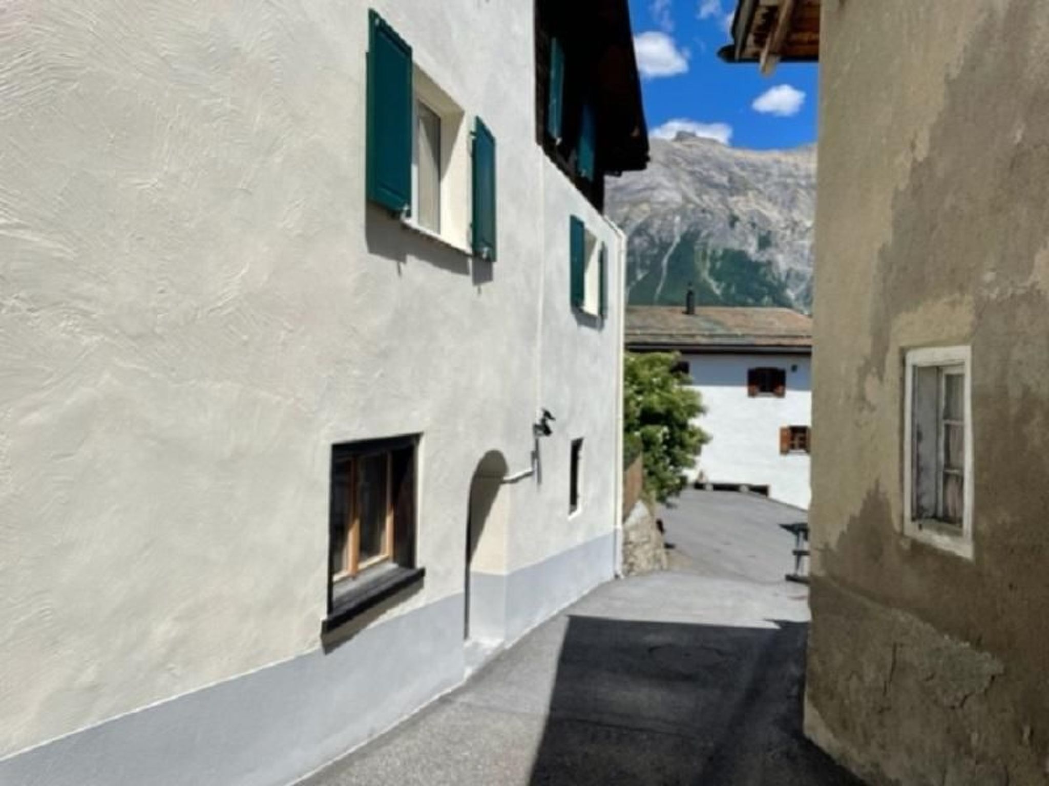 Una stretta via fiancheggiata da edifici, con una montagna sullo sfondo e un cielo sereno.