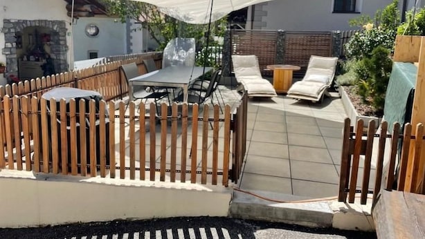 Un patio con cerco de madera, mobiliario exterior y un paraguas grande.