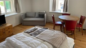 Una habitación acogedora con una cama, un sofá, una mesa de comedor con sillas y un televisor sobre un mueble de madera.