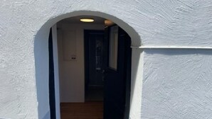 Un pasillo estrecho con piso de madera y un felpudo negro en la entrada.