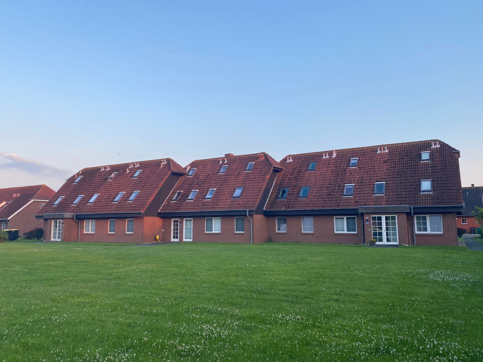 A row of red-roofed residential buildings with multiple windows and a green lawn in front.