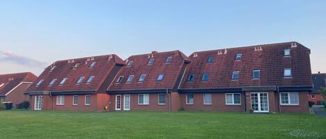 A row of red-roofed residential buildings with multiple windows and a green lawn in front.