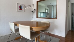 Un coin repas avec une table ronde en bois, quatre chaises, un grand miroir et un tableau encadré au mur.