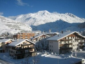 Une station de montagne enneigée, avec des bâtiments de style chalet, un ciel dégagé et une piste de ski en arrière-plan.