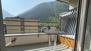 Un balcon avec une table en métal et des coussins à rayures, donnant sur un paysage montagneux.