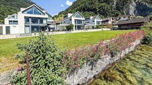 Moderni asuinalue, jossa on taloja, kirkas puro ja taustalla kohoava vuoristo.