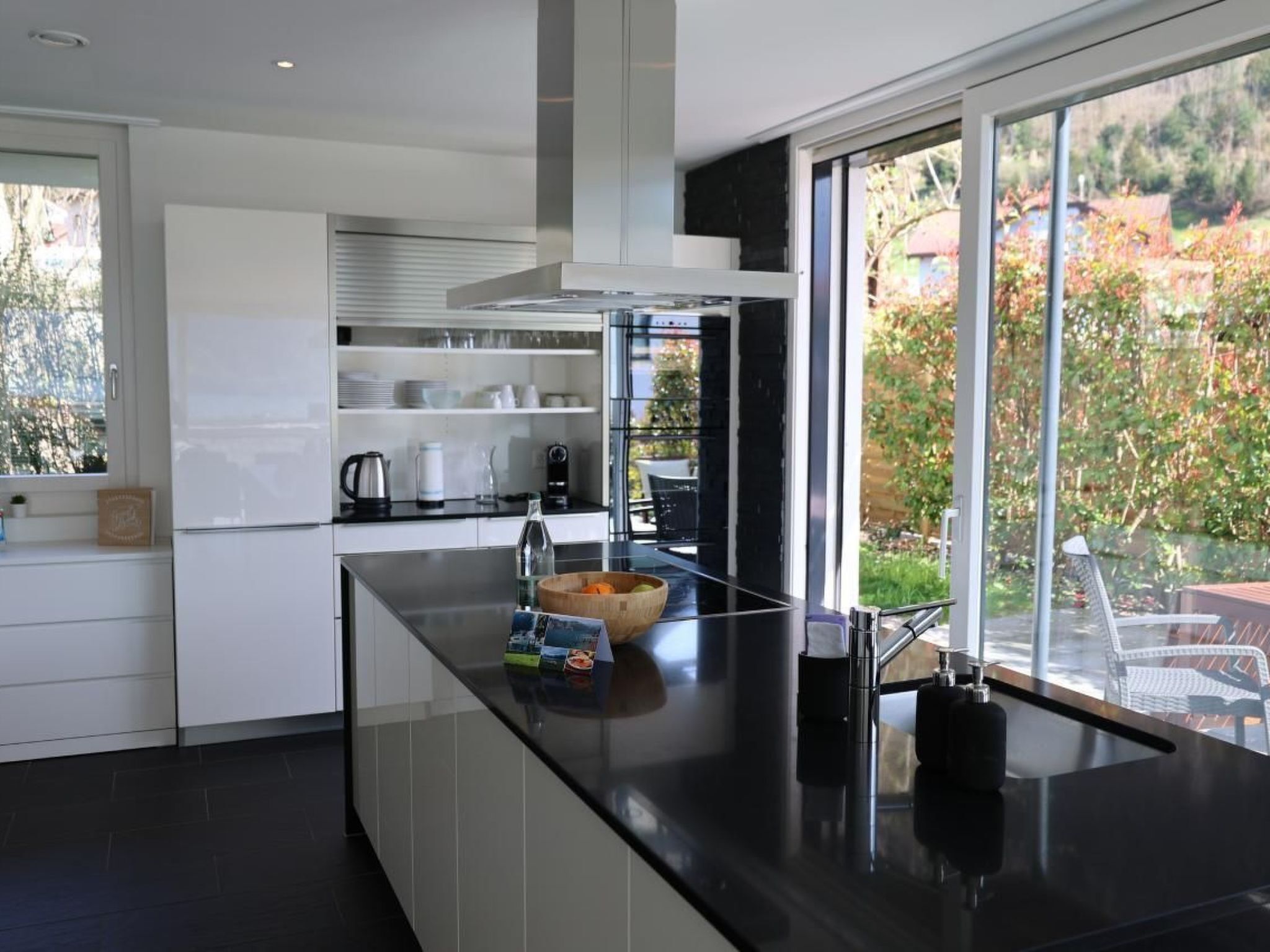 Una cocina moderna con encimera negra, armarios blancos y vistas al exterior a través de amplios ventanales.
