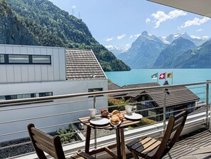 Een balkon met een ontbijttafel, met uitzicht op een meer en bergen.