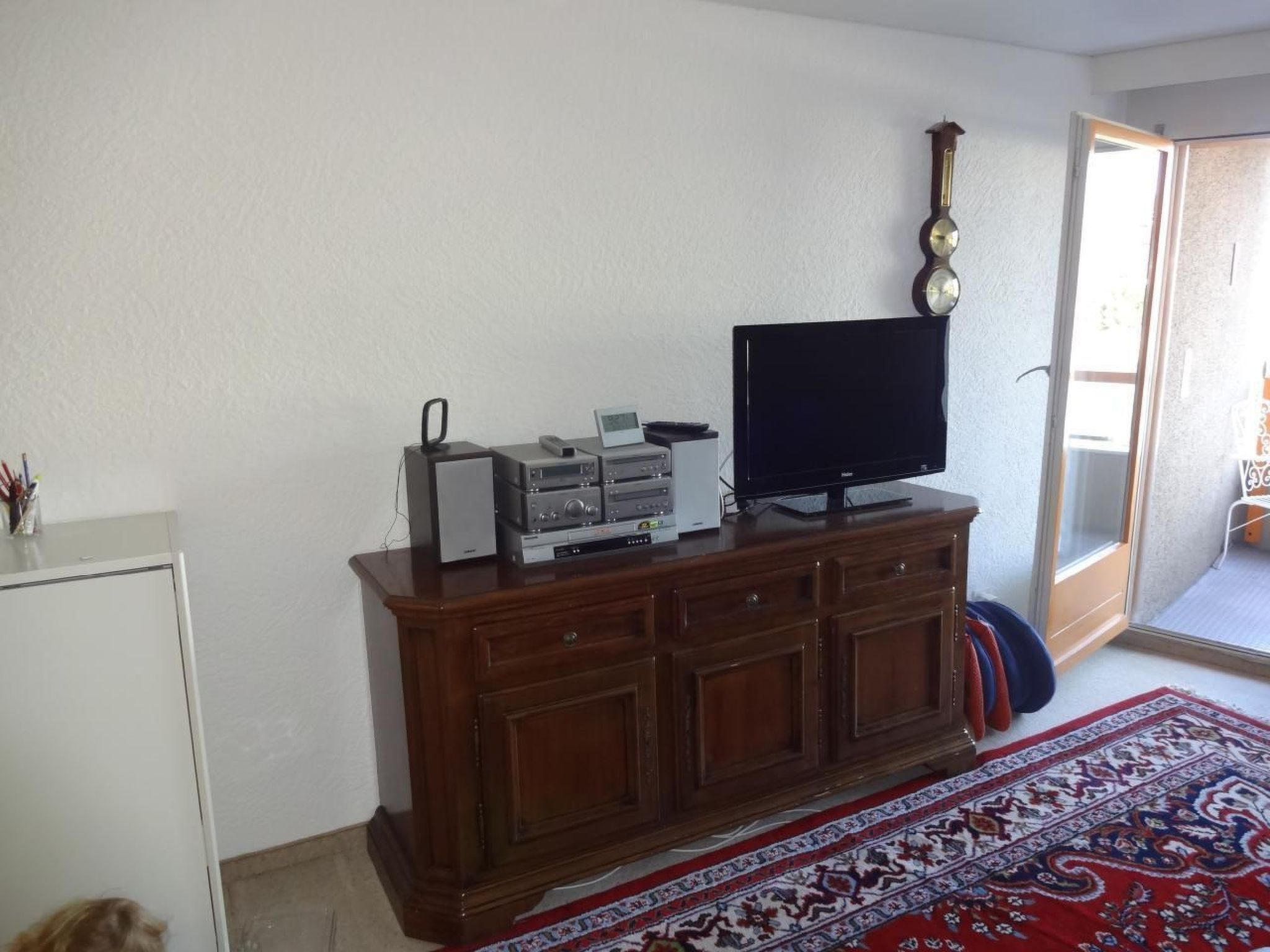 Una sala de estar con un mueble de madera, un televisor de pantalla plana y un reloj en la pared.