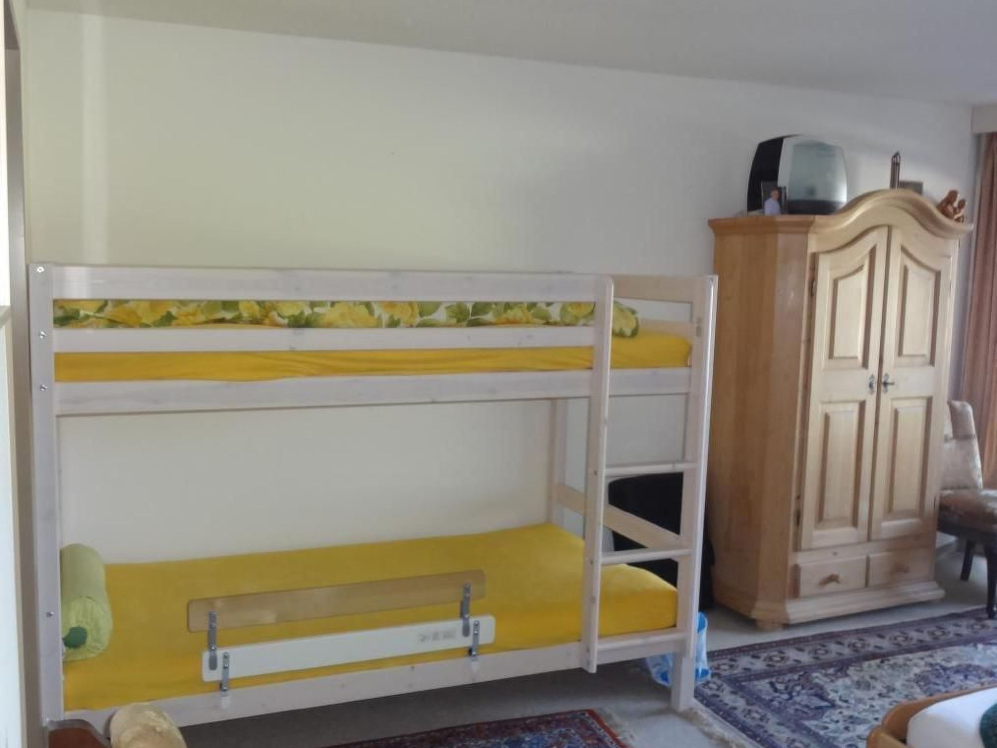 A bunk bed with yellow bedding, a wooden wardrobe, and a patterned rug.
