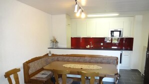 A dining area with a wooden table and chairs, a kitchen in the background with white cabinets and a red backsplash, and a tiled floor. - Wohnung mit herrlichem Blick auf den Pilatus by Interhome (Weggis)