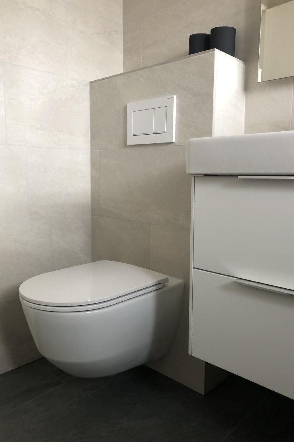 A modern bathroom with a white toilet, a white cabinet, and a light switch on the wall.