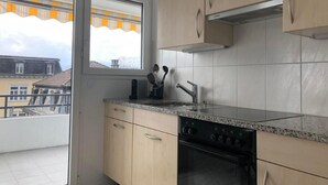 A kitchen with a stove, sink, and cabinets. There is a window with a view of buildings outside. - Studio "Rubi" Weggis by Interhome (Weggis)