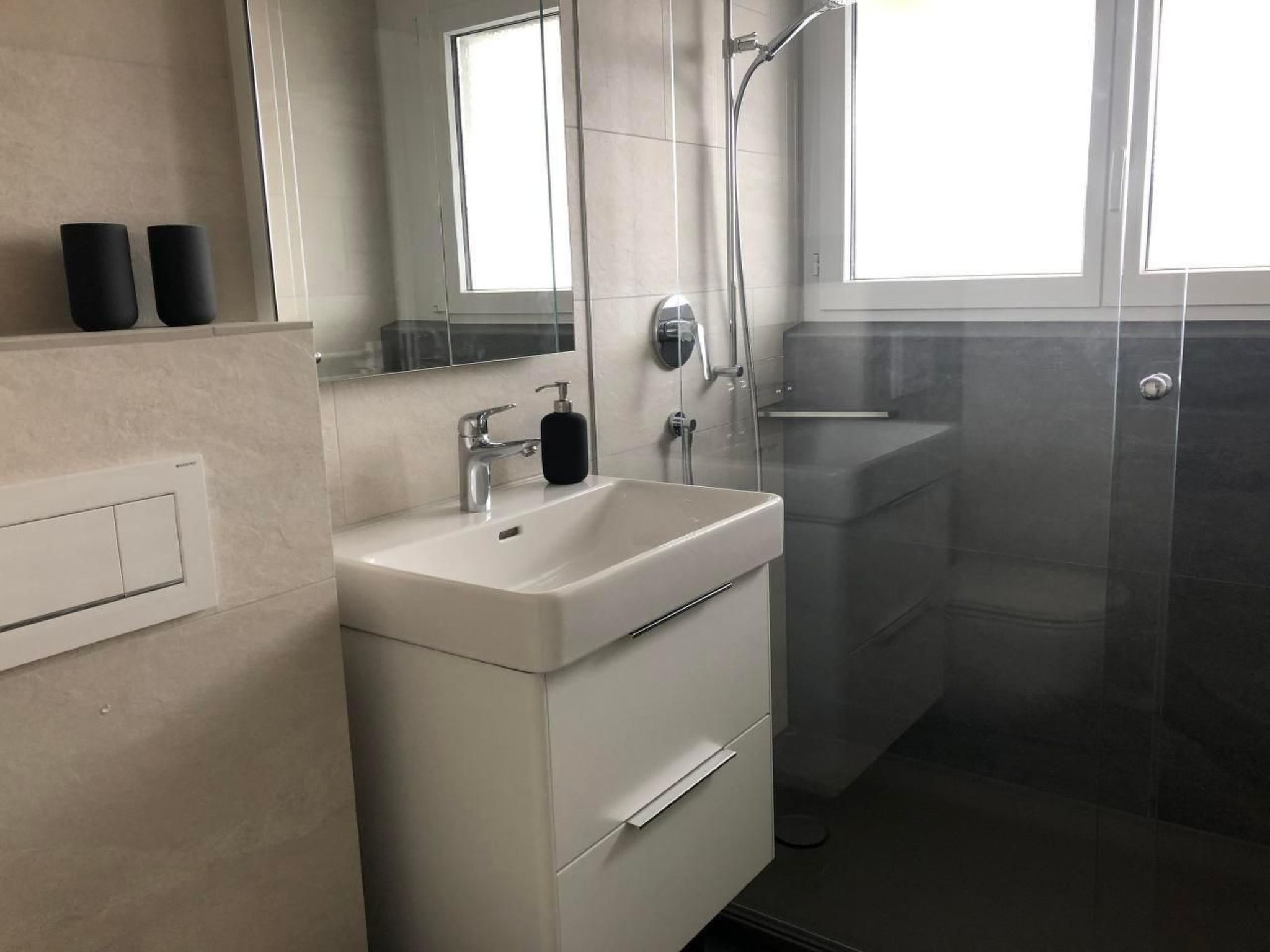 A modern bathroom with a white sink, a mirror, a shower, and a window.