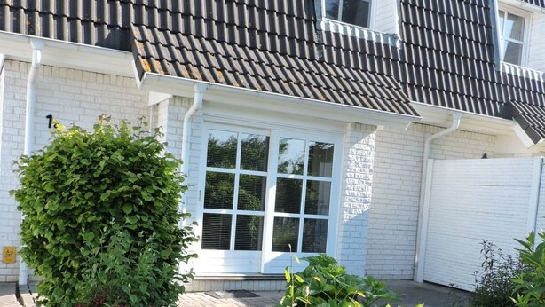 A house with a tiled roof, white exterior walls, a front door, and a small garden area with various plants. - Vacation home Sina by Interhome (Bannesdorf)