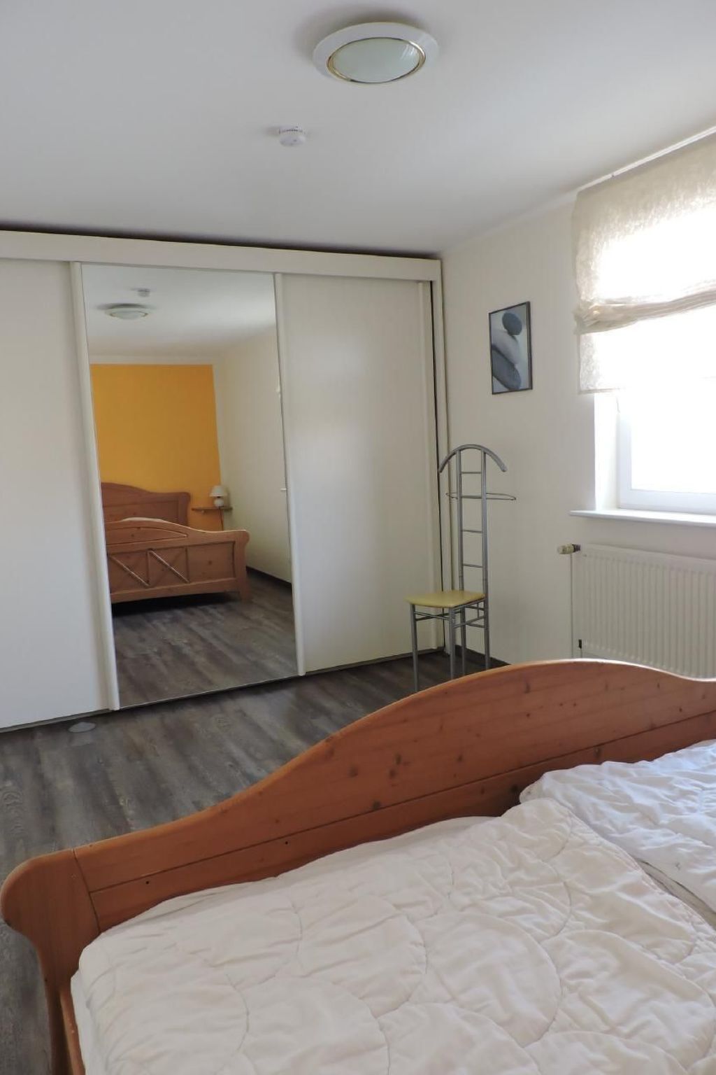 Een slaapkamer met een houten bed, een kledingkast, een radiator en een raam met gordijnen.