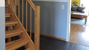 A wooden staircase leading to an upper floor, a dark tiled floor, and a room with a yellow wall and a sofa. - Vacation home Sina by Interhome (Bannesdorf)