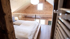 A cozy attic bedroom with a wooden ceiling, a bed with a white bedspread, a hanging light fixture, and a window providing natural light. - SPYCHER WEGGIS by Interhome (Weggis)