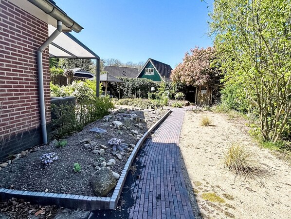 Ein Gartenweg führt zu einem Haus mit Backsteinfassade und einem grünen Dach.