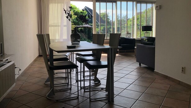 Un comedor con mesa y sillas, un radiador y vistas al exterior a través de amplios ventanales.