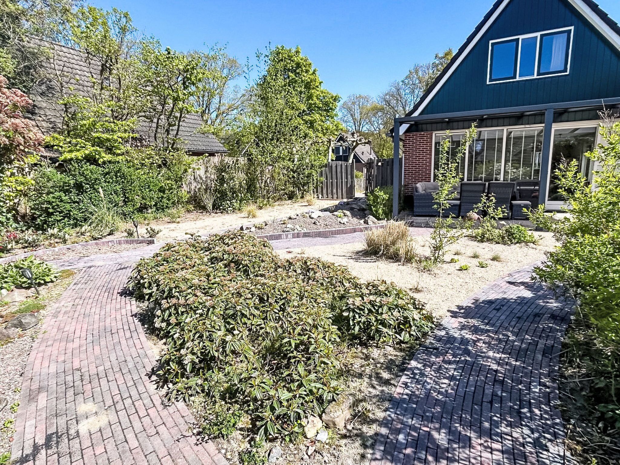 Un quartier résidentiel avec une allée pavée menant à une maison à l’extérieur bleu foncé et dotée de grandes fenêtres.