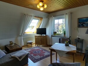 En hyggelig stue med et fjernsyn, møbler i træ, et mønstret tæppe og et billede på væggen.