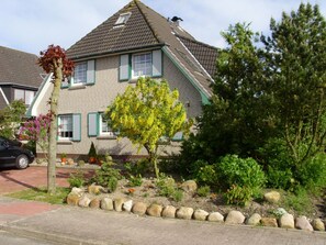 A two-story house with a sloped roof, green shutters, and a garden with various plants and flowers. - Apartment Antje by Interhome (Büsum)
