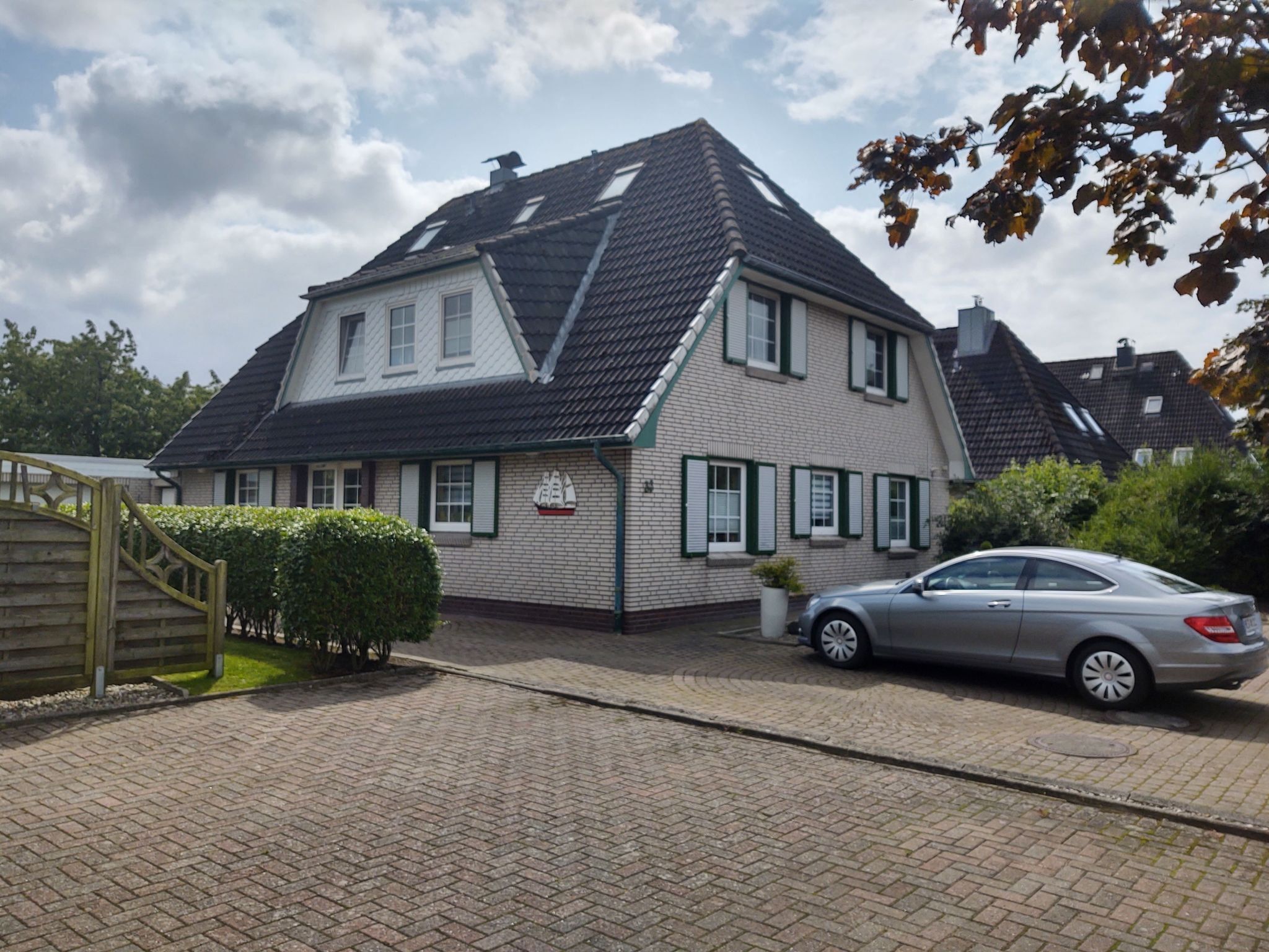 Une maison à deux étages, avec un toit en pente, une façade en briques et une voiture garée dans l’allée.