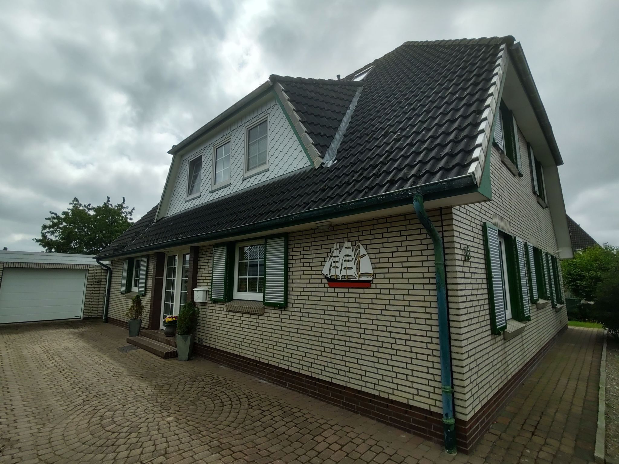 A two-story house with a tiled roof, a brick facade, and green shutters.