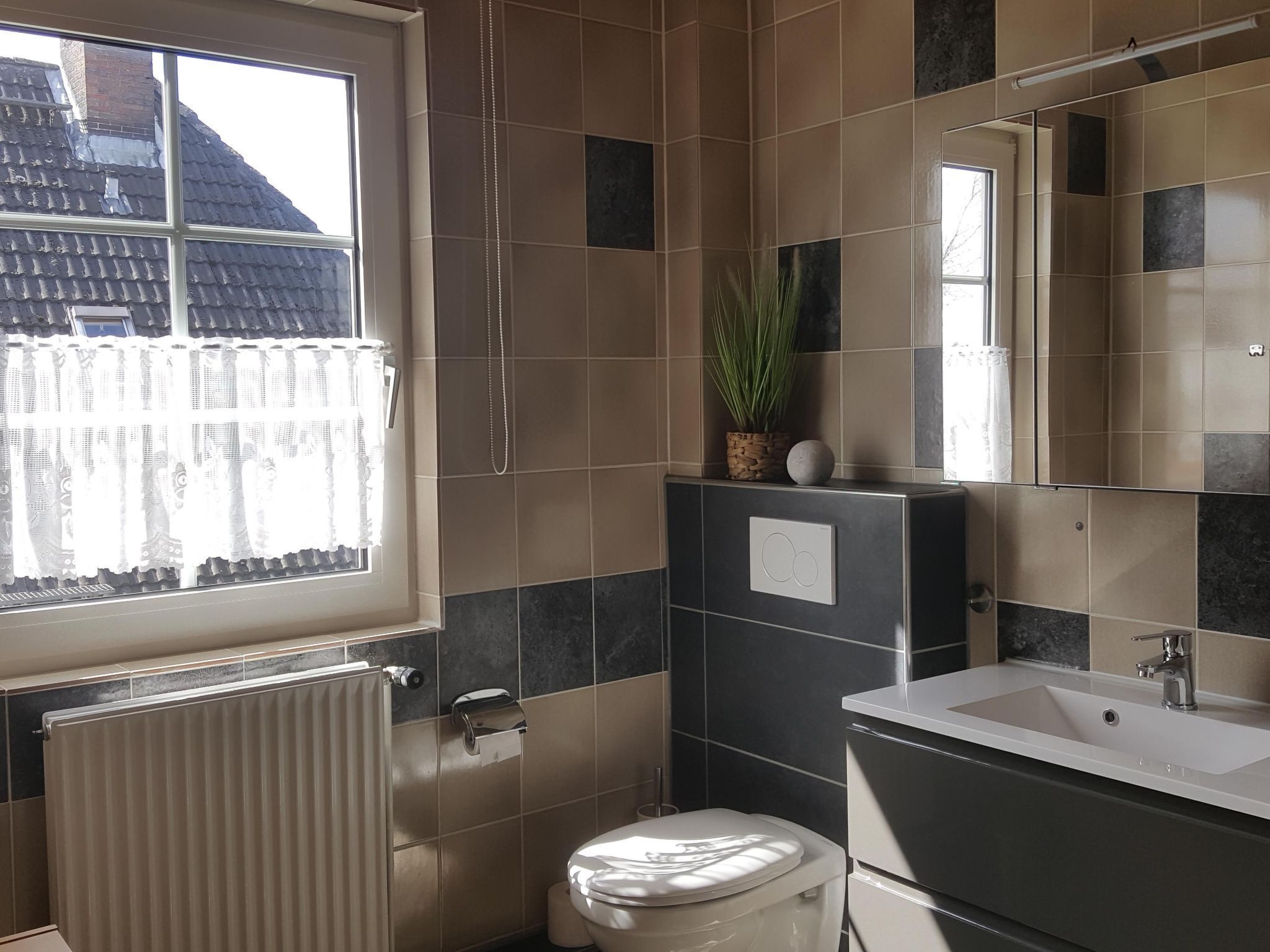 Une salle de bain avec des toilettes, un lavabo et un miroir. Il y a une fenêtre donnant sur un bâtiment à l’extérieur.