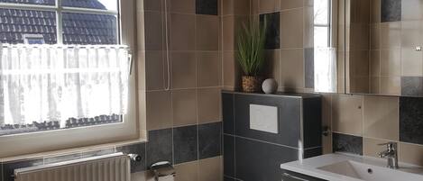 Une salle de bain avec des toilettes, un lavabo et un miroir. Il y a une fenêtre donnant sur un bâtiment à l’extérieur.