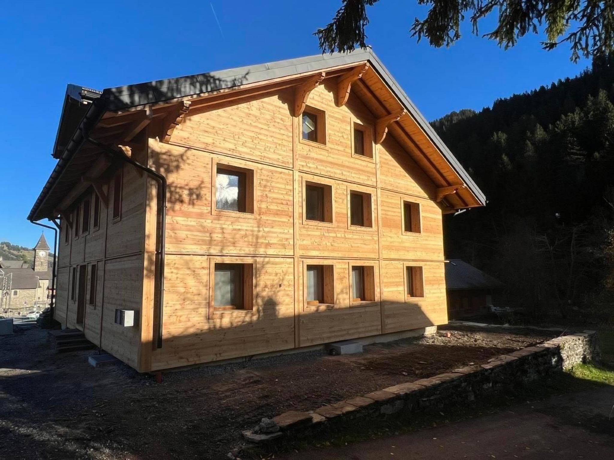 A multi-story wooden building with a sloped roof, multiple windows, and a stone foundation.